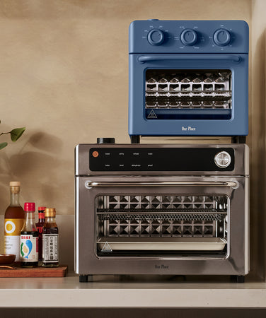 A modern kitchen countertop displays assorted foods, including pizza, muffins, hot dogs, fries, salad, and pastries, arranged around a stainless steel toaster oven.