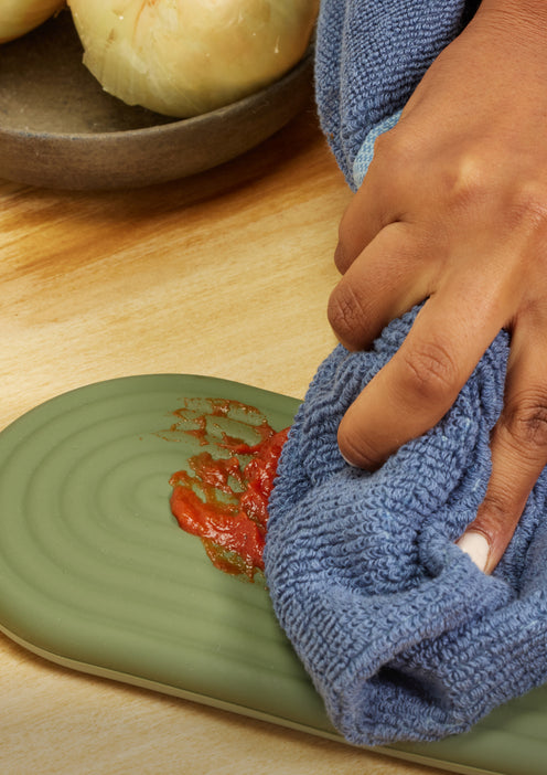A chef wipes sauce cleanly off the silicone part of green Hot Mitts 