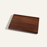 A rectangular wooden cutting board with a groove along the edges, placed on a plain light background. The bottom right corner features small engraved text.