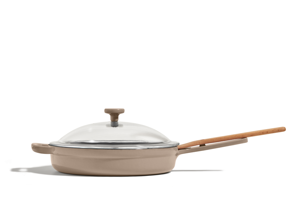 A beige ceramic skillet with a long wooden handle and a clear glass lid, shown on a white background.
