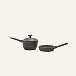 The Tiny Cookware Duo, featuring a black saucepan with lid and a matching black frying pan, are placed side by side against a plain light background.