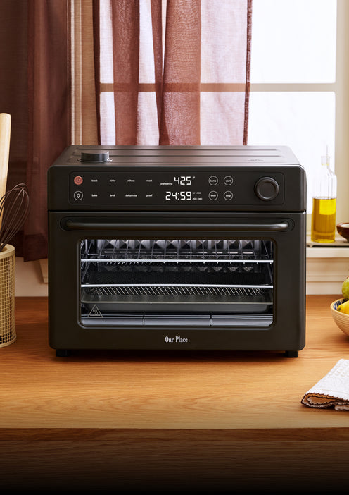 Black Our Place countertop oven with a digital display showing 425 degrees and a 24:59 timer, sitting on a wooden kitchen counter.