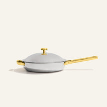 A silver stainless steel Titanium Always Pan Pro 10.5″ 2.0 frying pan with a matching lid and gold-toned handles and knob.